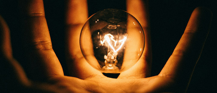 Hand holding a glowing light bulb, representing electricity pricing and energy innovation